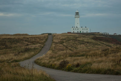 Lighthouse on field by building against sky