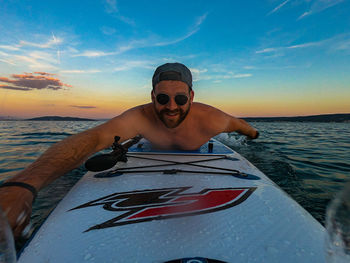 Portrait of man swimming in sea against sky during sunset