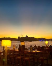 Silhouette cityscape by sea against clear sky during sunset