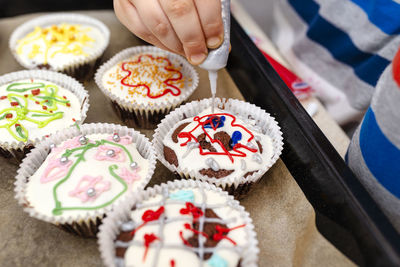 A child squeezes colored frosting from a tube onto chocolate brown cupcakes covered.