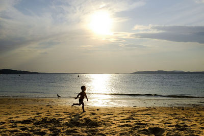 Silhouette boy running at beach against sky during sunset