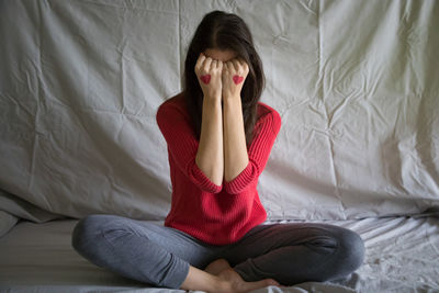 Depressed woman with heart shapes on hands sitting at bedroom