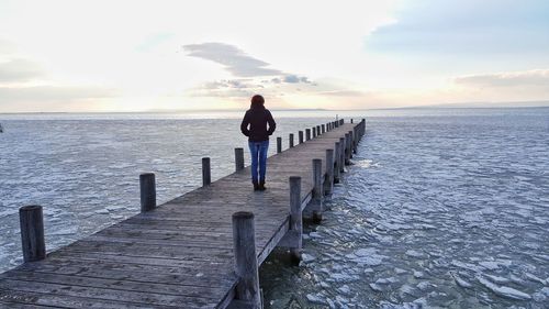 Woman standing on pier against sky during sunset