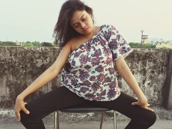 Portrait of beautiful young woman sitting against wall