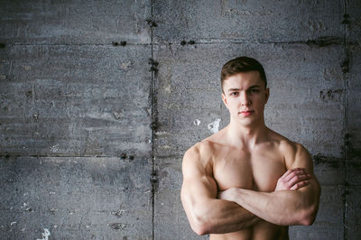 Close-up portrait of shirtless muscular man standing by wall