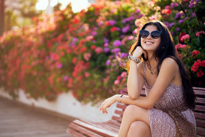 A woman is sitting on a bench in a park, wearing sunglasses and a dress person
