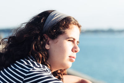 Side view of thoughtful teenage girl looking away while sitting against sea