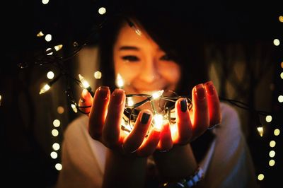 Smiling young woman holding illuminated lighting equipment in darkroom