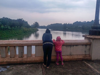 Rear view of women standing on railing against sky