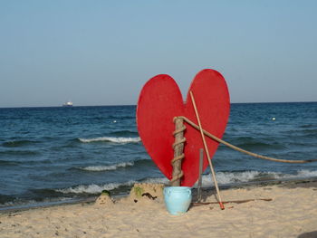 Red heart shape on beach against clear sky