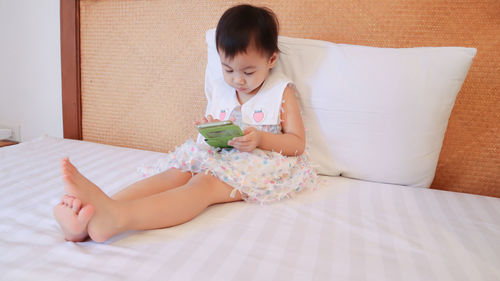 Cute girl using mobile phone while sitting on bed at home