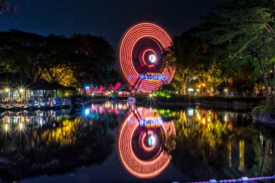 Illuminated ferris wheel by lake at night