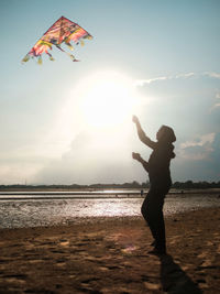 Silhouette woman with arms outstretched standing at beach against sky during sunset