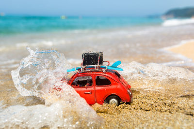 Red toy car on beach by sea against sky