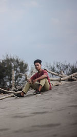 Portrait of man sitting on sand against sky