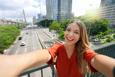 Beautiful smiling girl takes self portrait with ponte estaiada bridge in sao paulo, brazil.