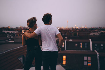 Rear view of couple standing against cityscape during sunset