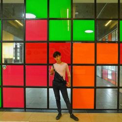 Full length of young man standing against glass wall