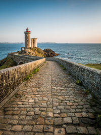 Footpath leading towards lighthouse by sea against sky