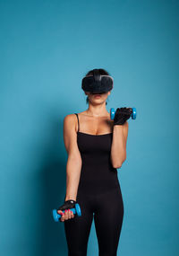 Portrait of young woman with arms raised standing against blue background