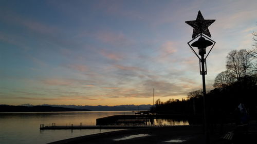 Silhouette street light by lake against sky during sunset