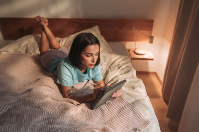 Portrait of young woman using mobile phone while lying on bed at home