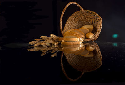 Close-up of breads with wheat and wicker basket on table against black background