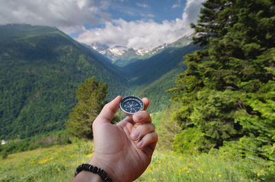 A man holds a compass in his hand against the backdrop of nature, a green forest and mountains in