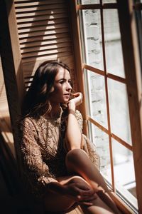 Thoughtful young woman looking through window at home