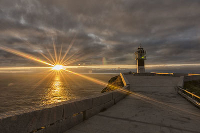 Lighthouse by sea against sky during sunset