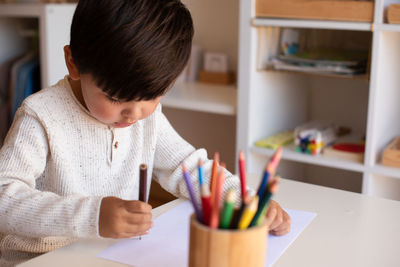 Cute boy drawing on paper at home