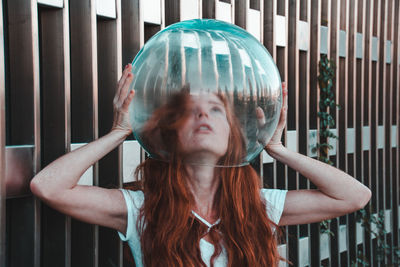 Close-up of young woman removing glass helmet from head against metallic railing