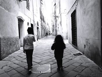 Rear view of women walking on footpath amidst buildings