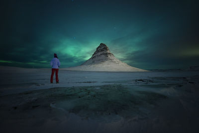 Rear view of woman standing on beach by mountain against sky