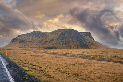 Scenic view of mountain by road in valley against dramatic sky during sunset