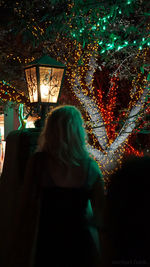 Rear view of silhouette woman in illuminated christmas tree at night