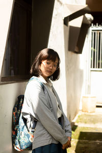 Portrait of young woman standing against building