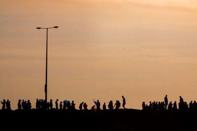 Silhouette people on street against sky during sunset