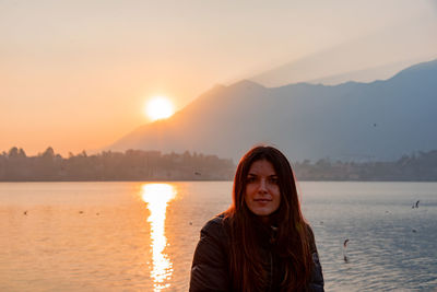 Portrait of young woman against lake during sunset