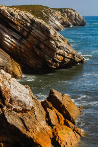 Scenic view of sea and waves hitting a rocky cliff