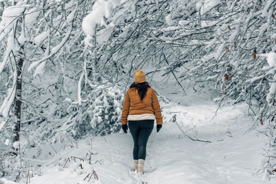 Rear view of girl wearing winter clothes, walking on snowy path in forest