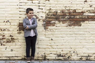 Boy looking away while standing against brick wall