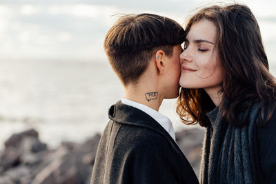 Lesbian women embracing while standing against sea