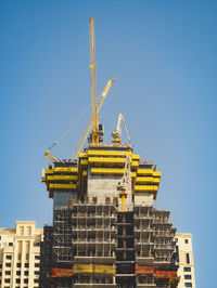 Low angle view of crane by building against clear blue sky