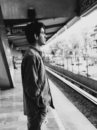 Side view of young man standing at railroad station