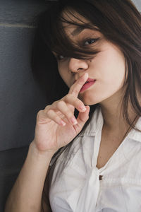 Portrait of young woman with finger on lips standing by wall