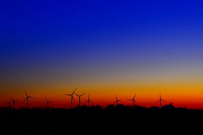 Silhouette wind turbines against orange sky