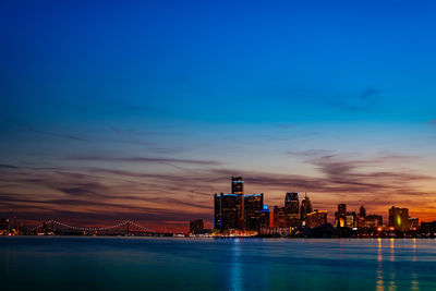 Illuminated buildings by sea against sky at night