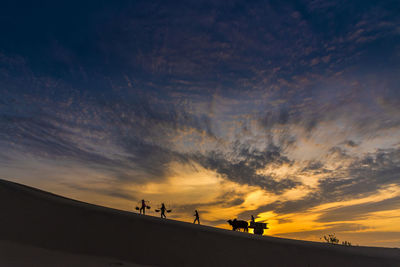 Silhouette people on land against sky during sunset