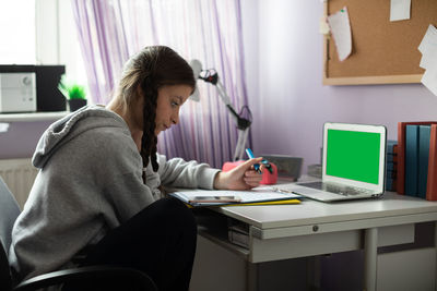 Green screen. a student sits at a desk doing schoolwork.